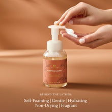Hand holding a pump bottle of pumpkin laurel soap with a brown background