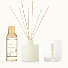 thymes Goldleaf home fragrance set with diffuser, reeds, and candle on a tan background