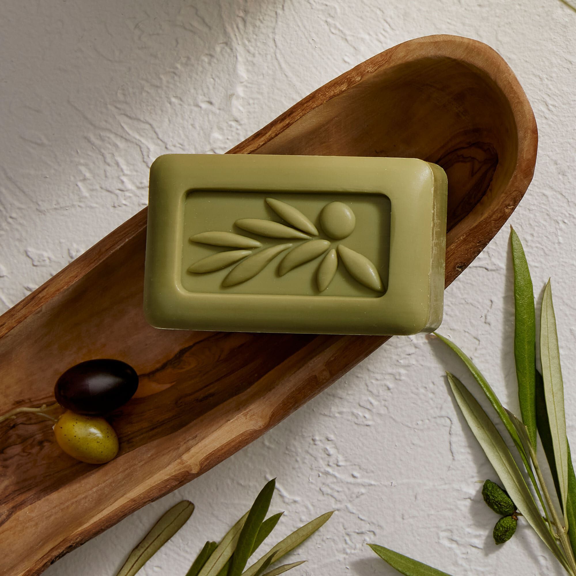 A bar of Thymes Olive Leaf soap with botanicals and olives.