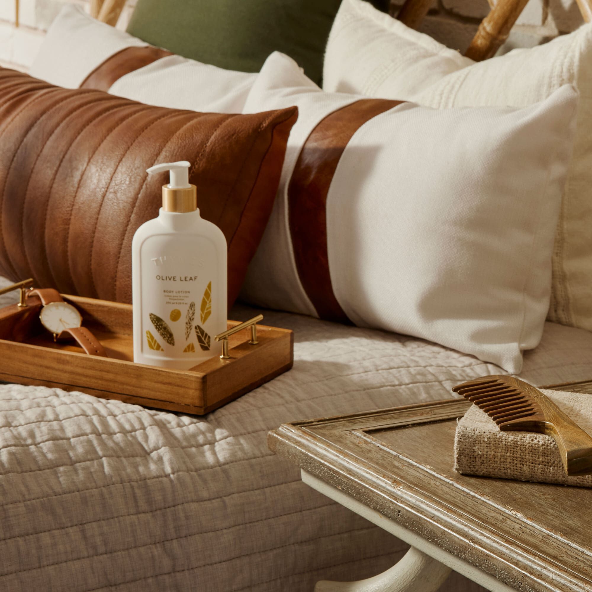 Thymes Olive Leaf Body Lotion on a tray atop a bed