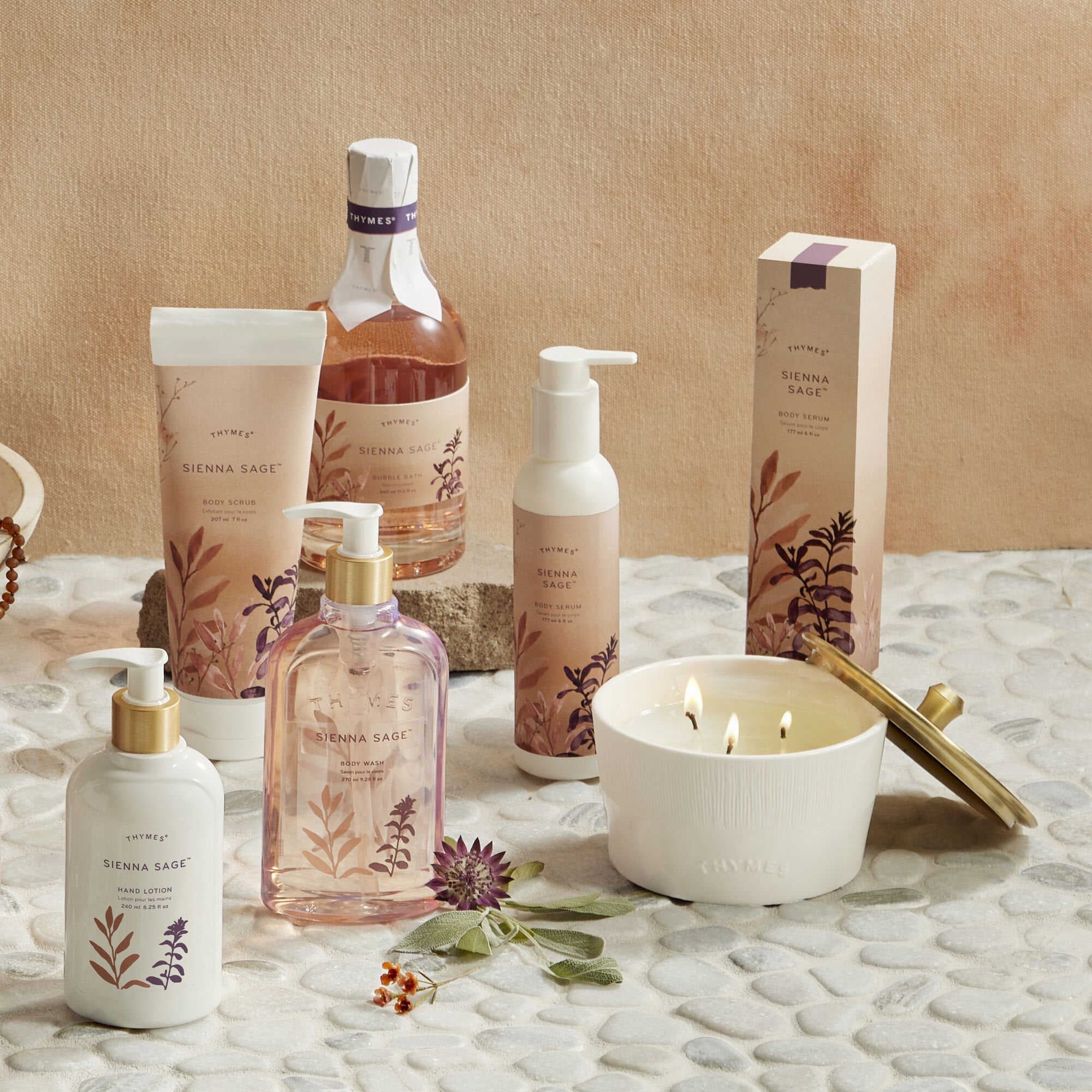 Thymes Sienna Sage products on a table, including a candle, body wash, hand lotion and bubble bath