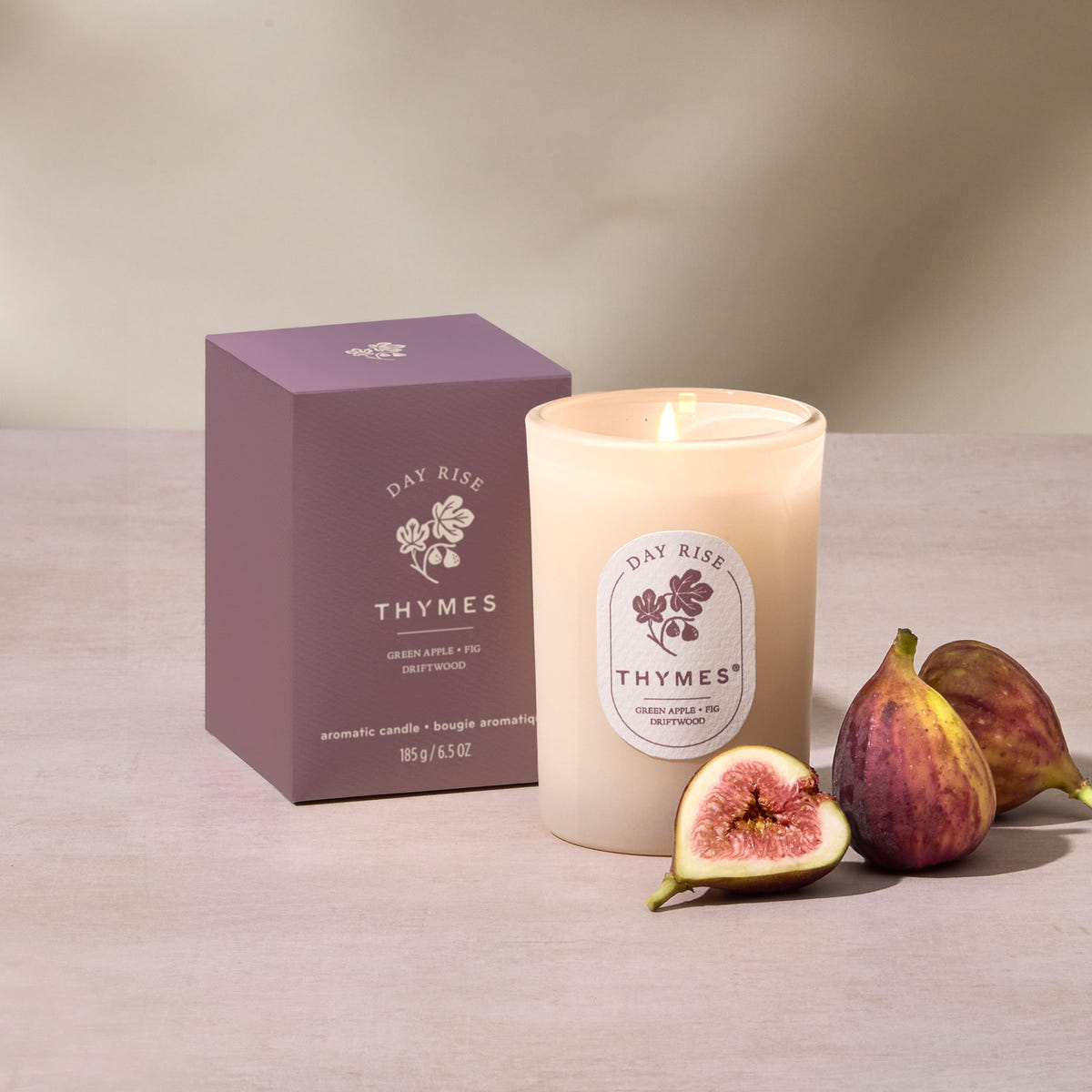 Alternate image of Thymes candle with packaging and figs on a neutral background