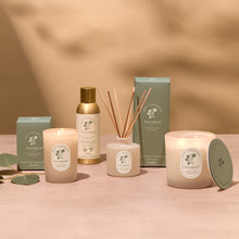 Thymes product line including candles, diffuser, and bottle on a pink surface with a beige background