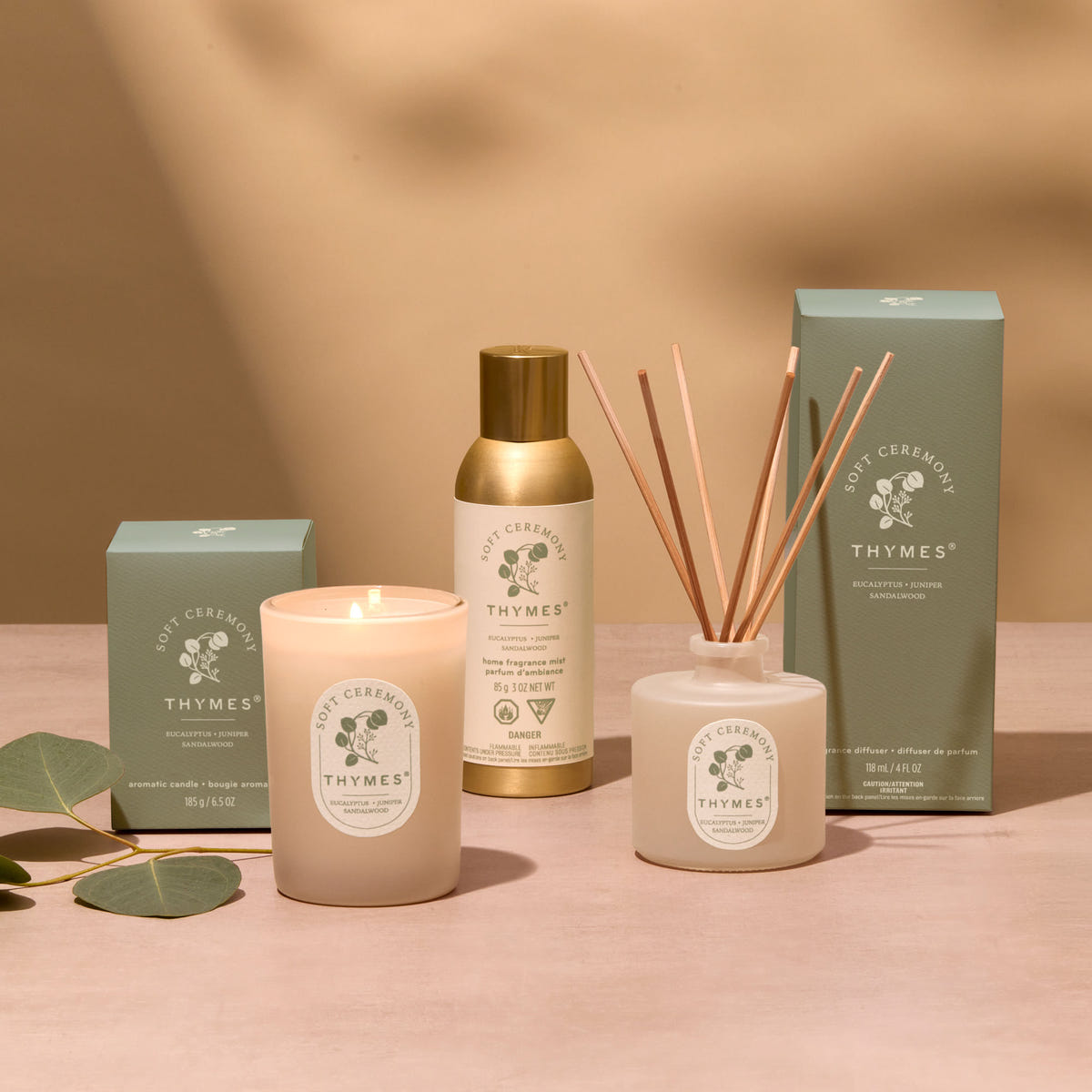 Alternate image of Thymes product line including a candle, diffuser, and boxes on a pink background