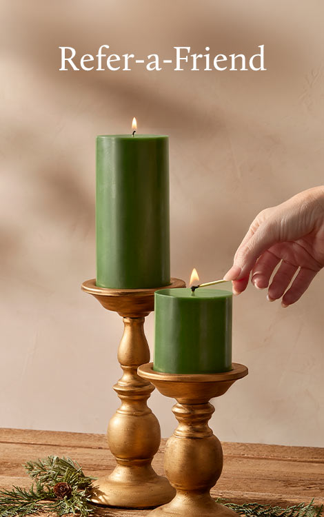 Two green candles in wooden holders with a hand lighting one candle against a beige background.