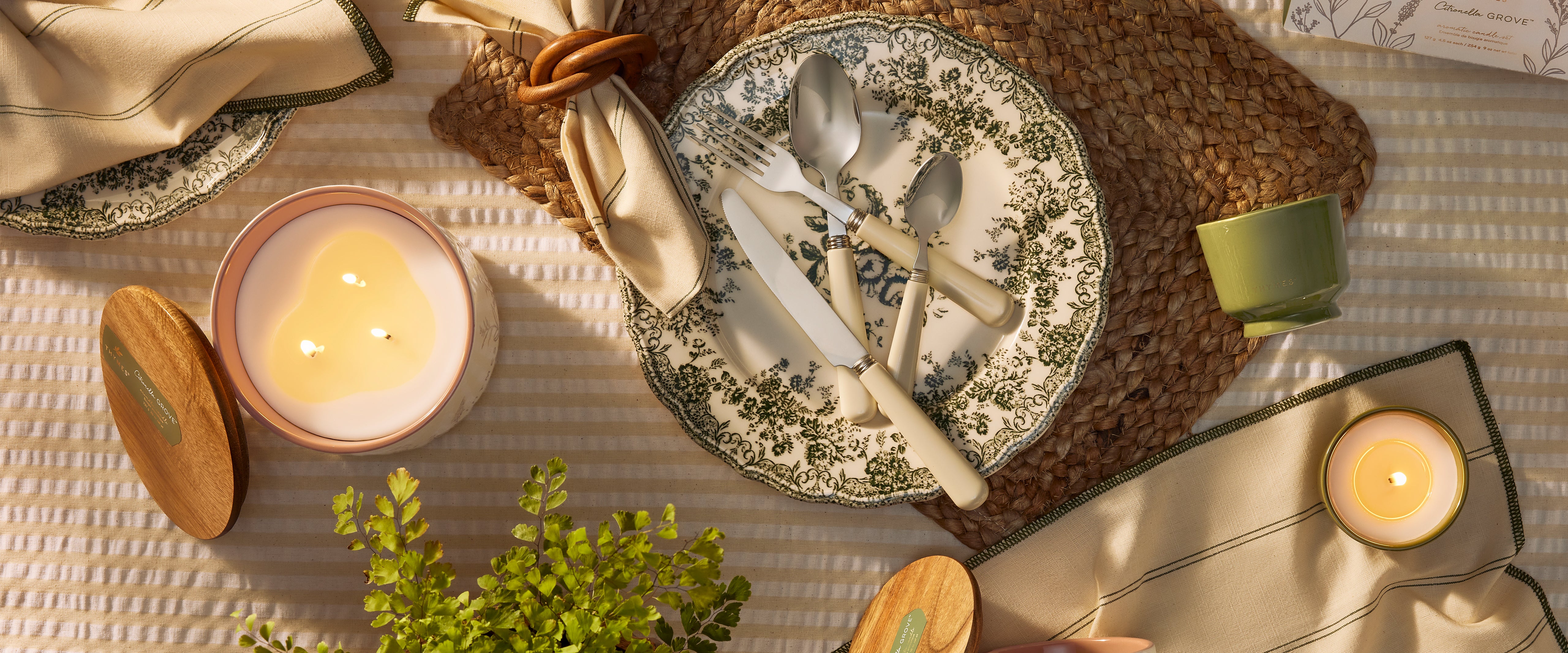 Dining table setting with plates, cutlery, candles, and a plant on a textured surface.