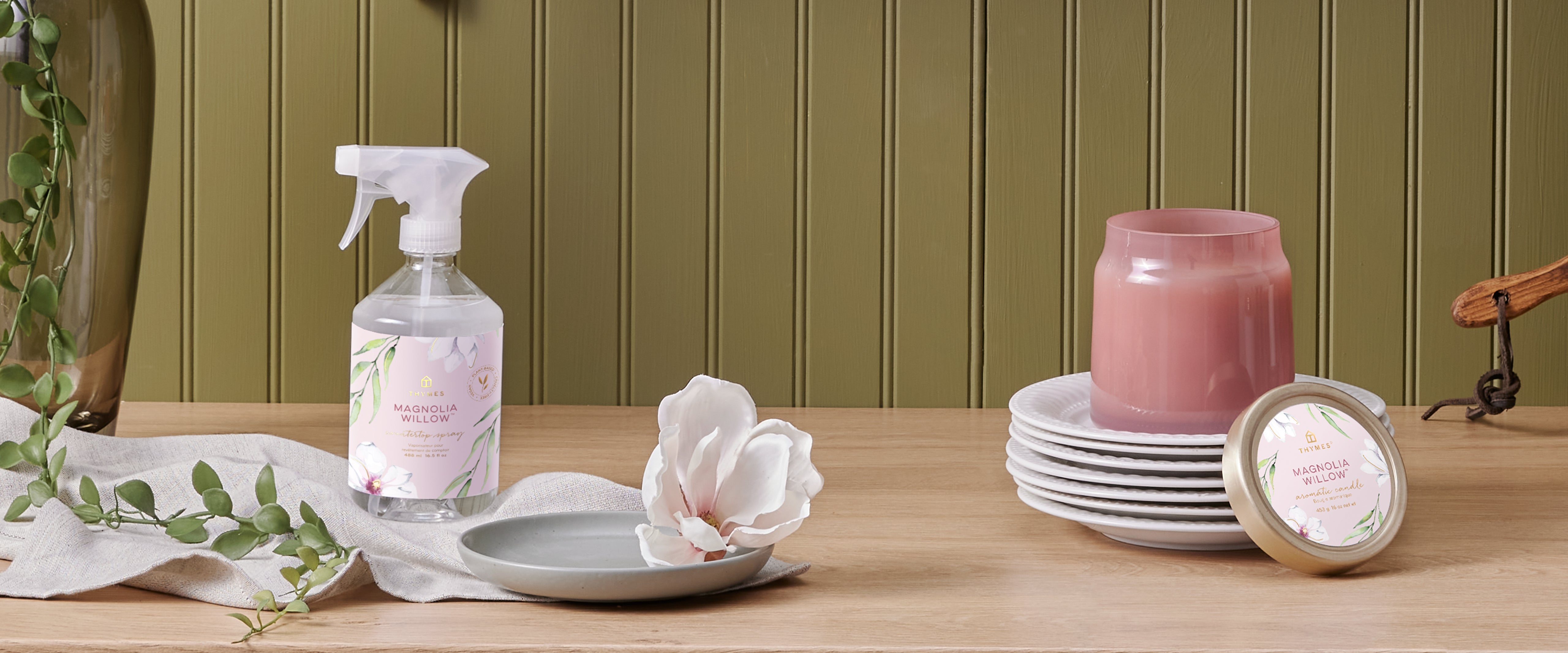 Cleaning spray bottle, pink candle, and decorative items on a wooden surface with a green paneled wall background.