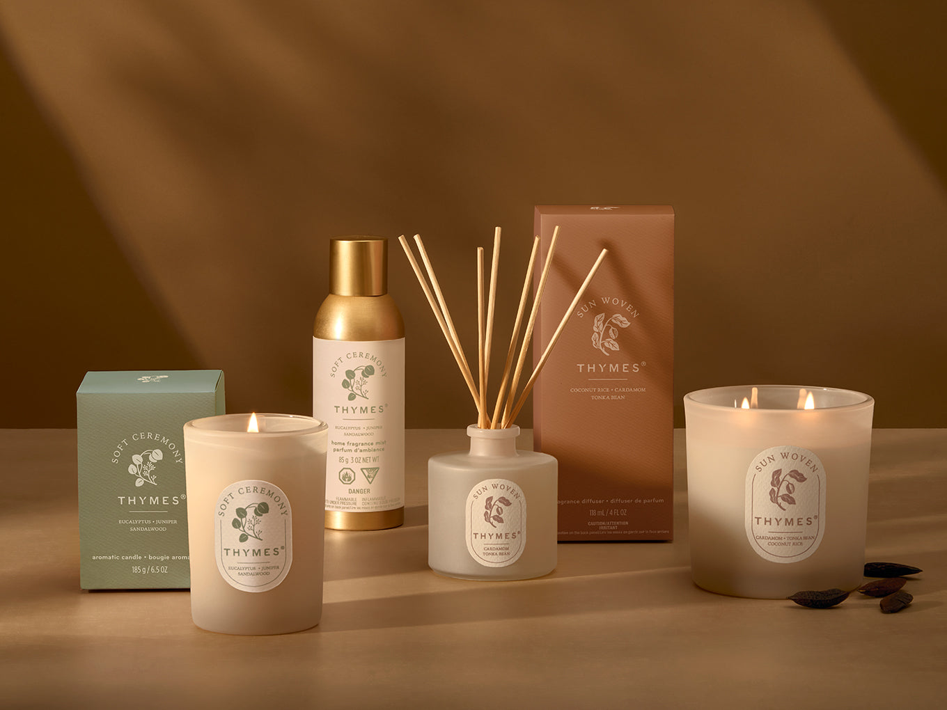 Collection of Thymes products including candles, diffuser, and boxes on a brown background