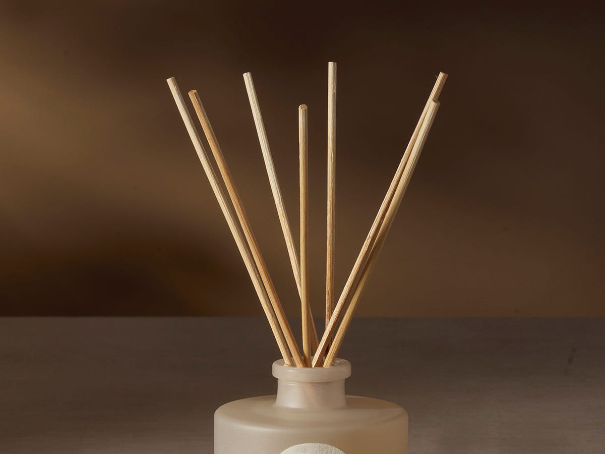Reed diffuser with wooden sticks in a white container on a dark background