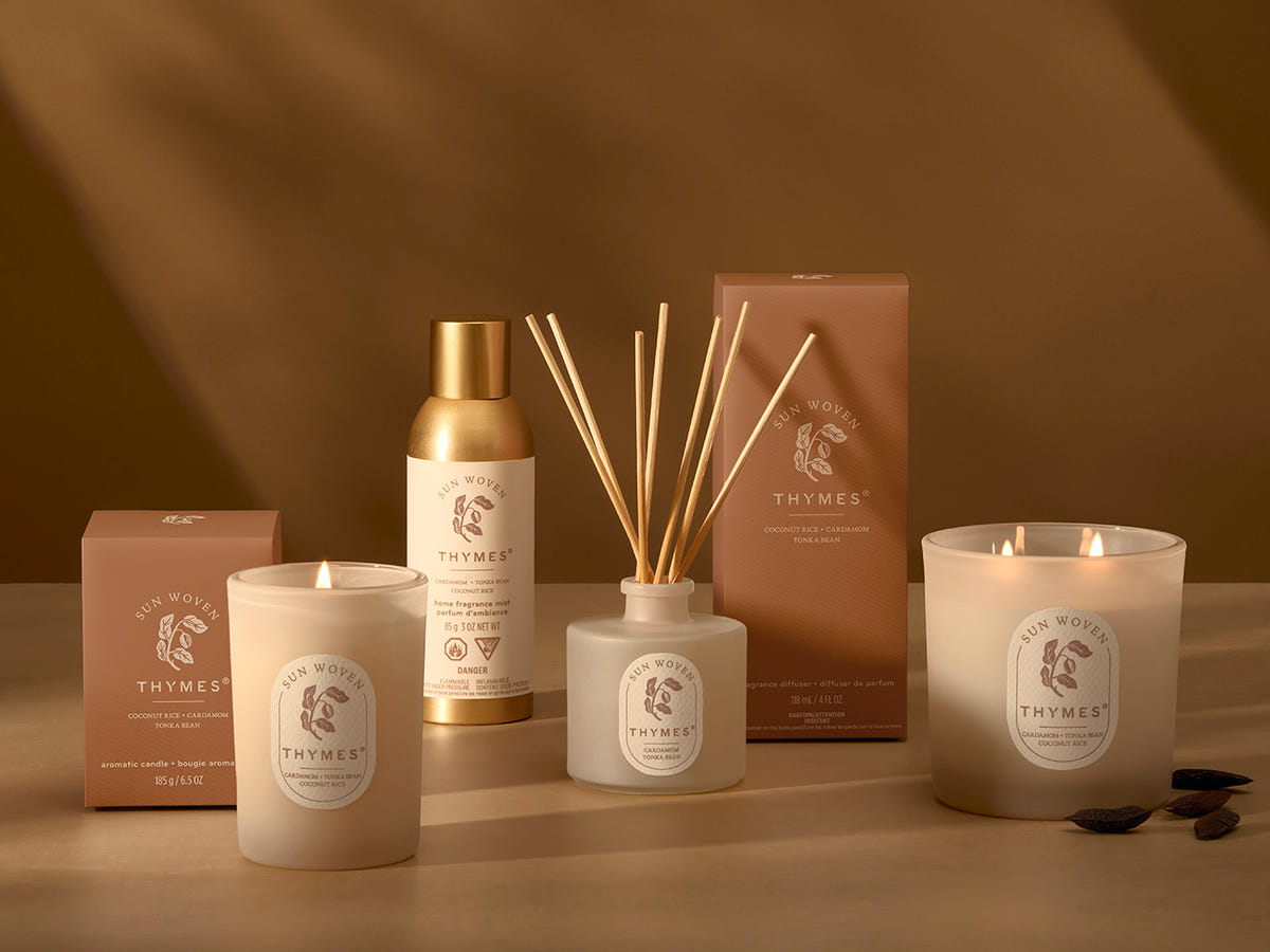 Collection of Thymes products including candles, diffuser, and bottle on a brown background