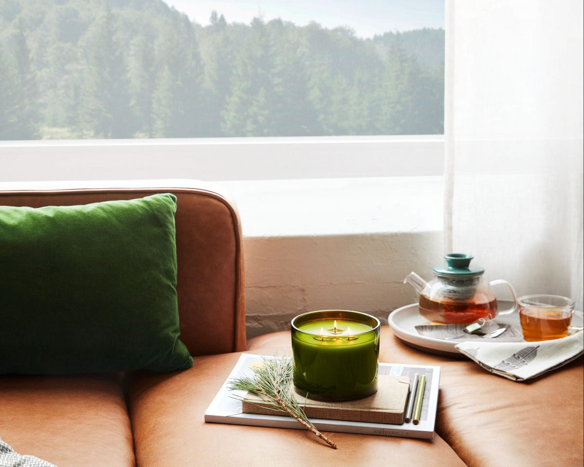 Candle and tea set on a couch with a scenic view outside the window
