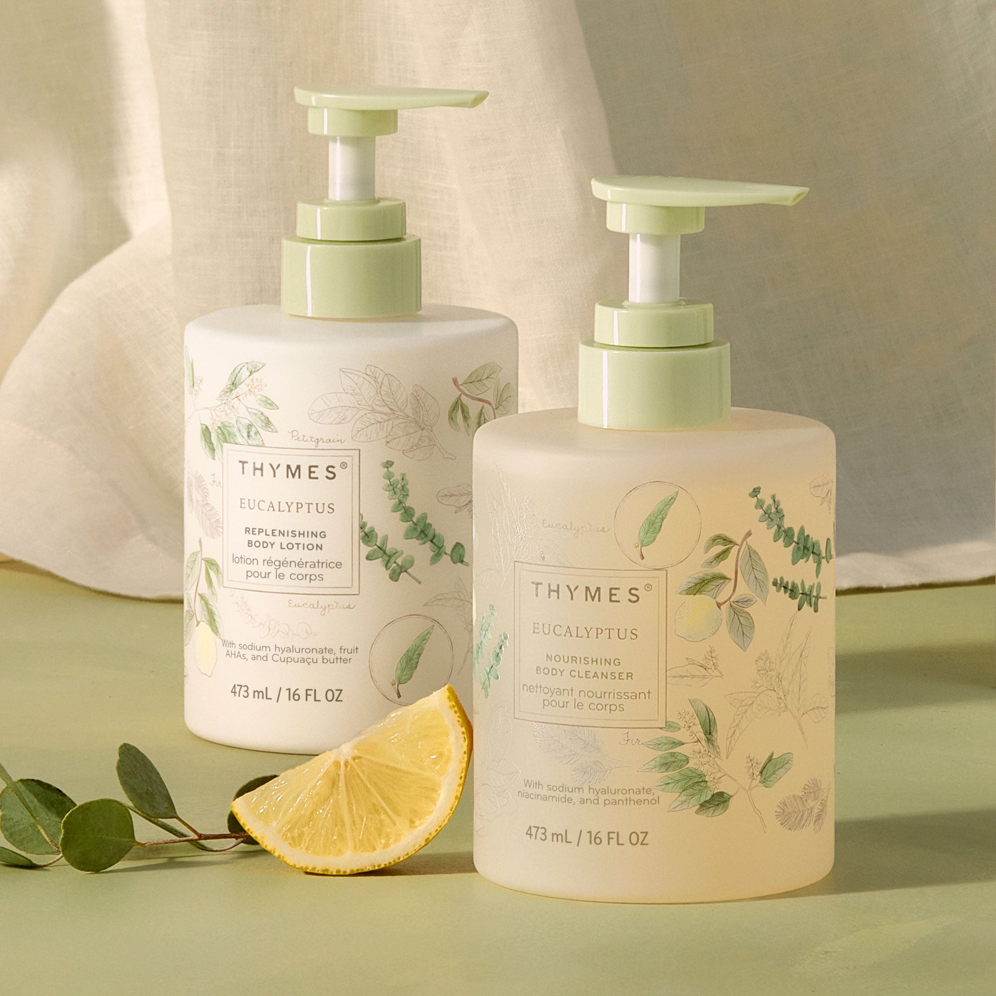 Two Thymes Eucalyptus body wash and body lotion bottles with a lemon wedge on a green background
