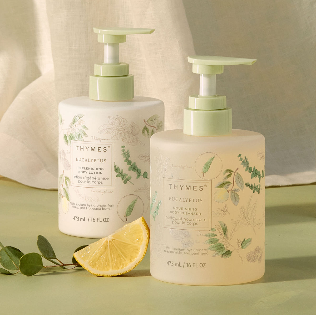 Two Thymes Eucalyptus body wash and body lotion bottles with a lemon wedge on a green background
