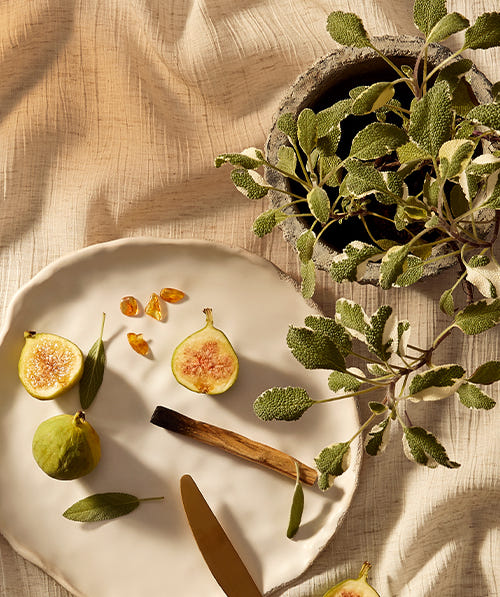 Fig sliced in half on a plate surrounded by sandal wood and sage plant