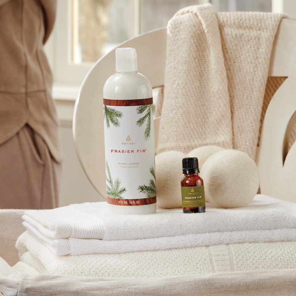 Thymes Frasier Fir Fabric Softener laundry care on top of folded linens next to Frasier Fir Wool Dryer Balls and Fragrance Oil