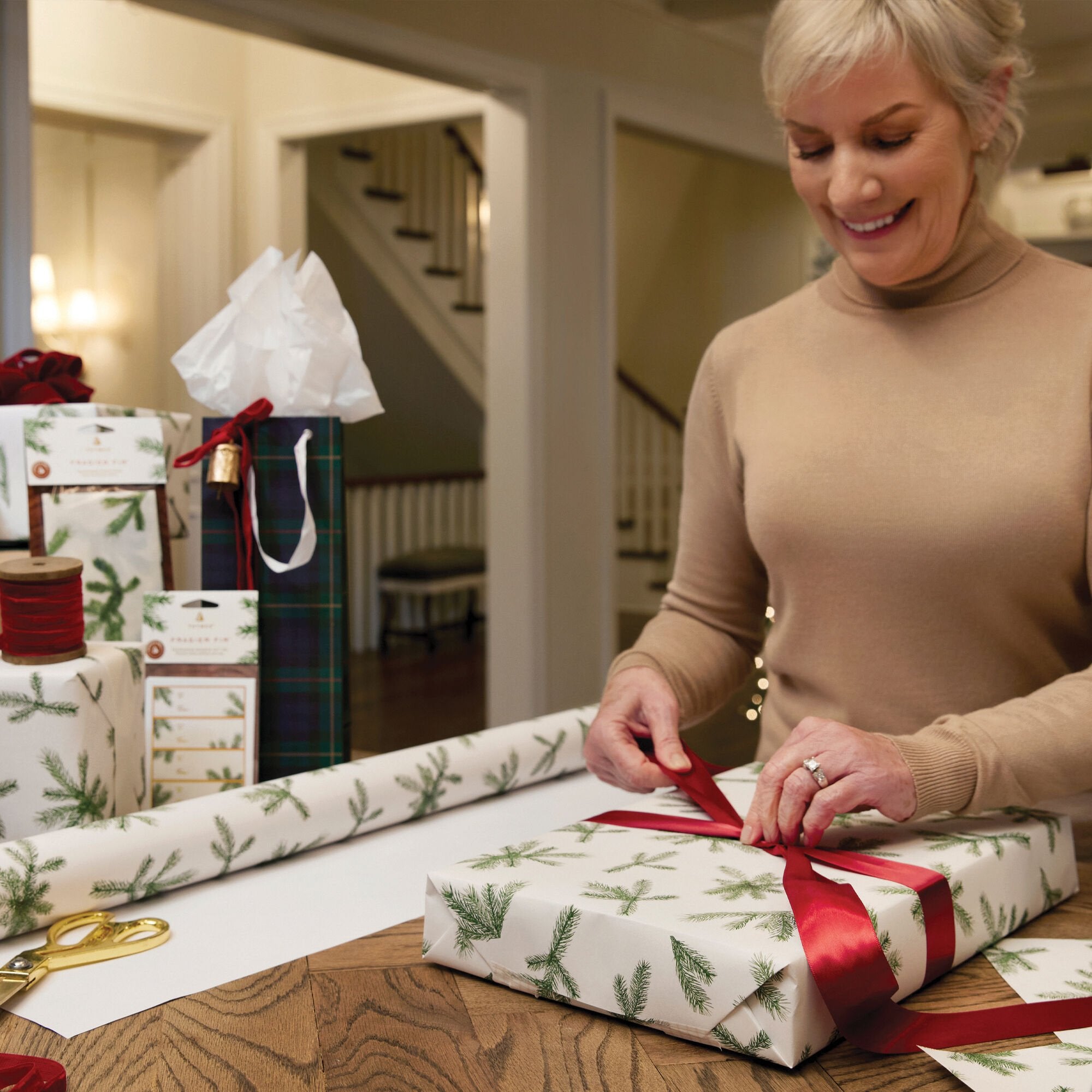 Gift being wrapped with Thymes Frasier Fir Fragranced Wrapping Paper adding a bow