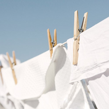 White clothes hanging on a line with wooden clothespins against a clear blue sky.