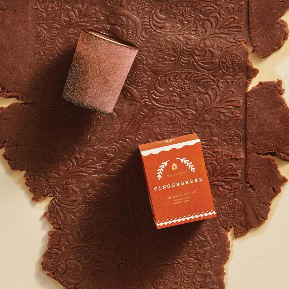 Alternate image of Thymes Gingerbread Votive Candle laying on decorative gingerbread batter