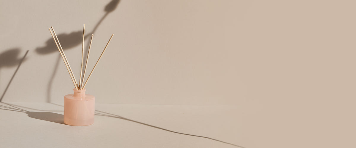 Pink ceramic diffuser with wooden reeds on a beige background