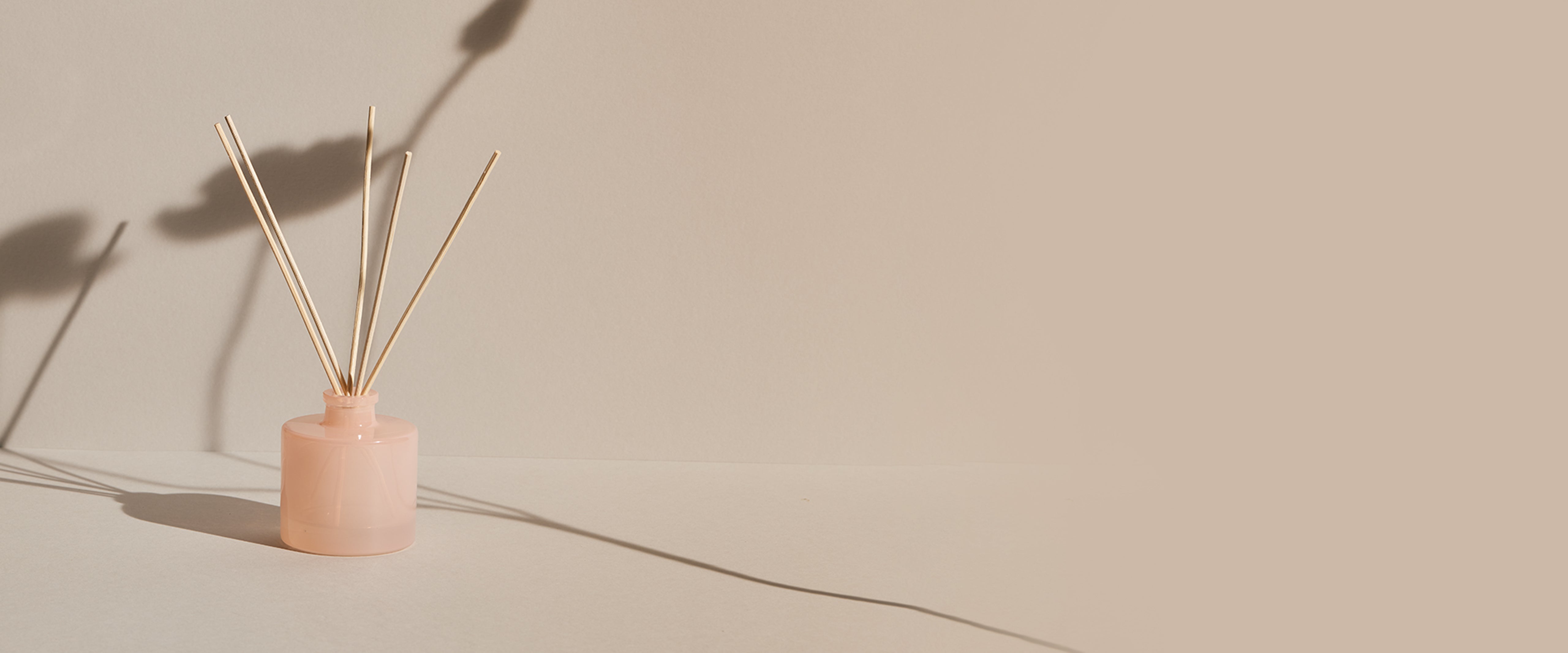 Pink ceramic diffuser with wooden reeds on a beige background