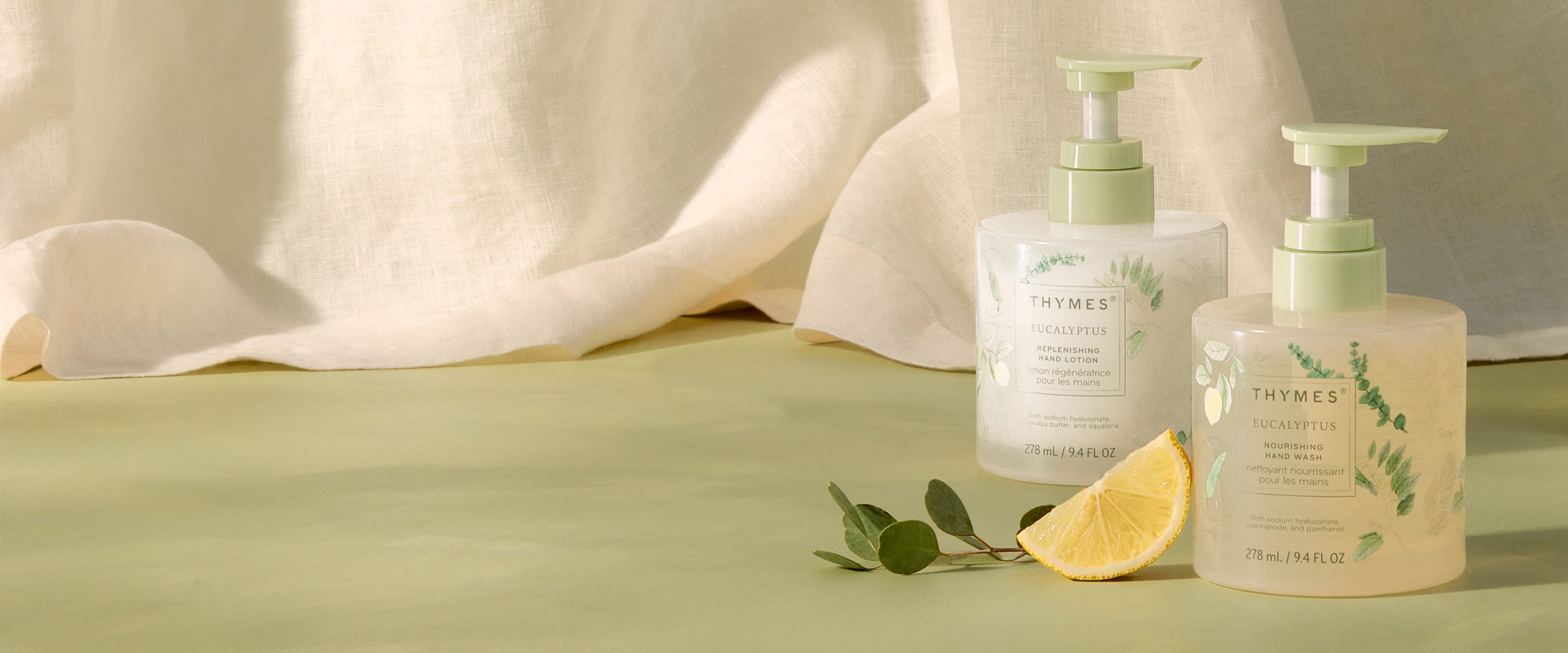 Two skincare bottles with a lemon and leaves on a soft fabric background