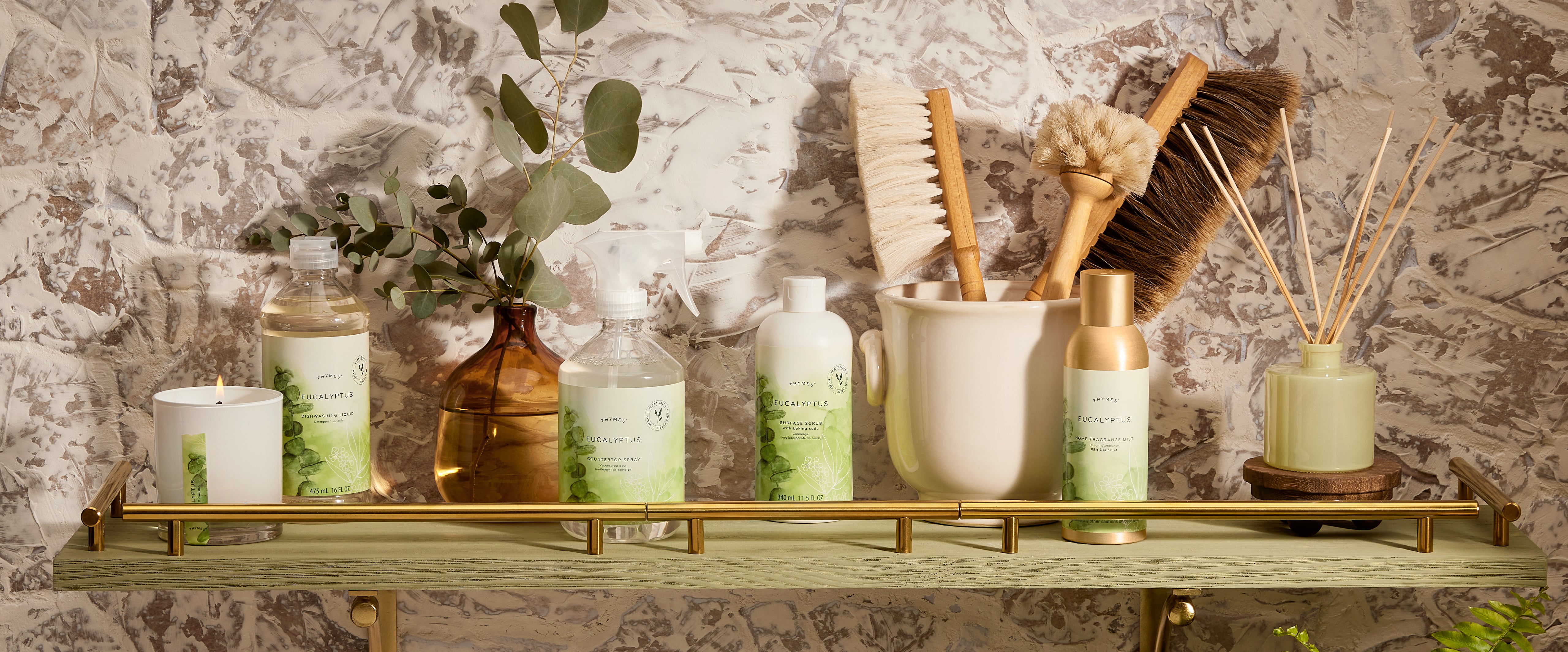 Set of cleaning tools and decorative items on a wooden shelf against a textured wall.