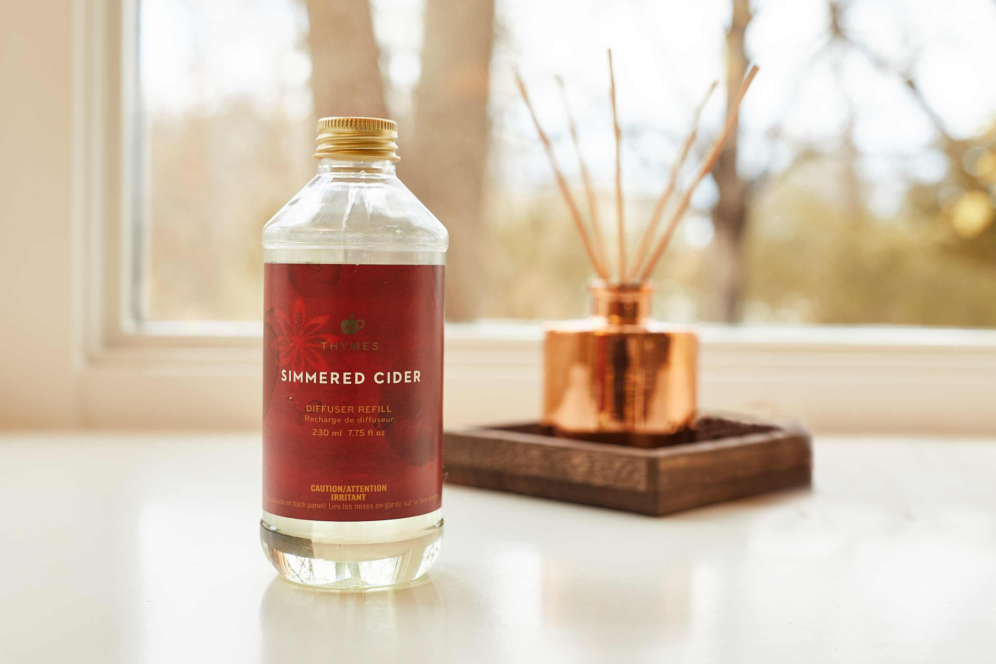 Bottle of 'Sweetened Cider' reed diffuser oil refill on a windowsill with decorative elements.