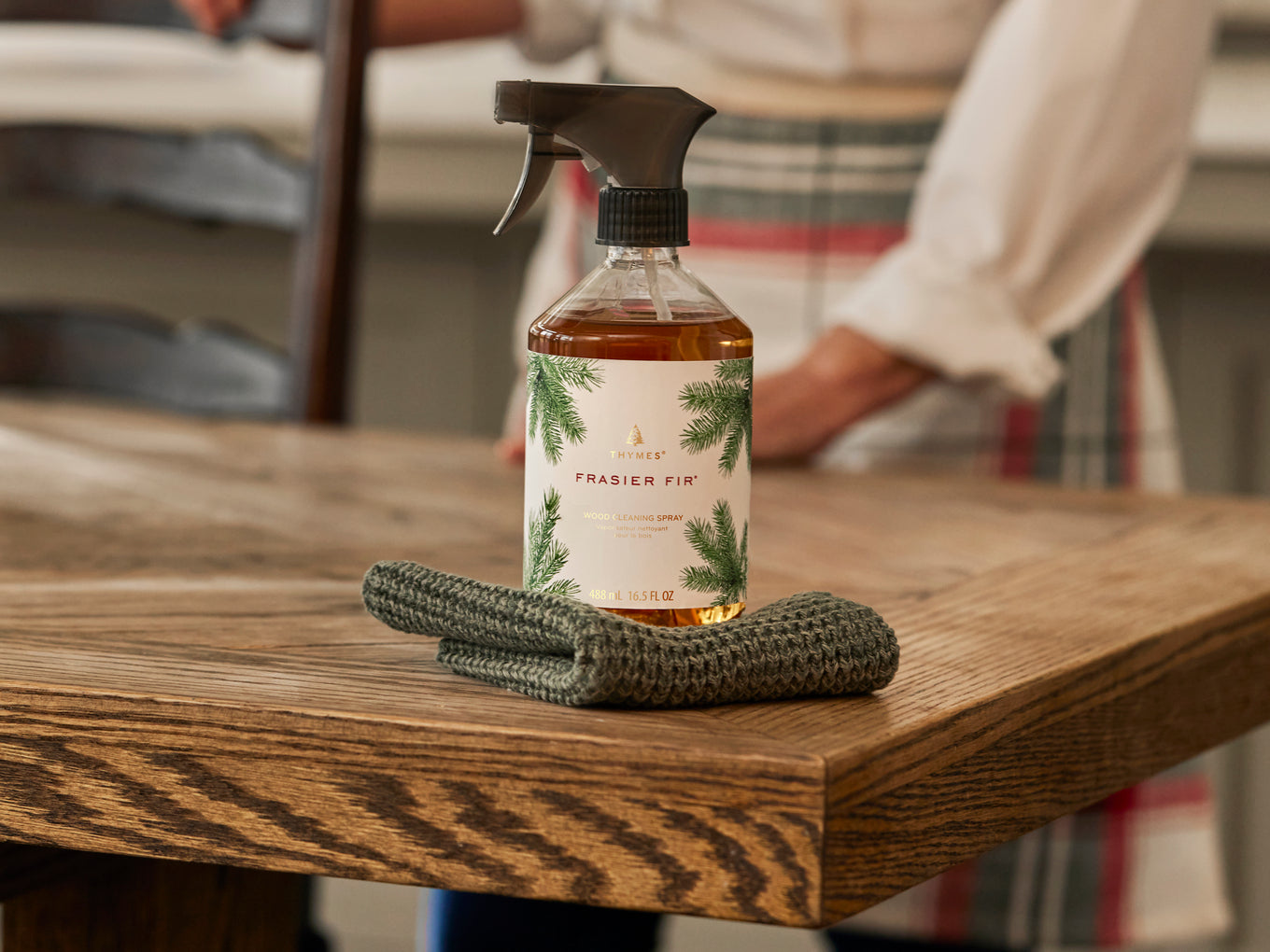 Frasier Firwood cleaning spray bottle with a label on a wooden surface, with a person in the background.