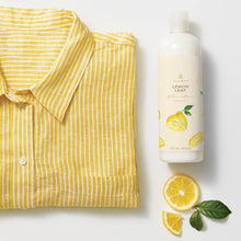 Thymes Lemon Leaf Fabric Softener to Soften Clothing with Citrus Scent next to yellow shirt and lemon slices