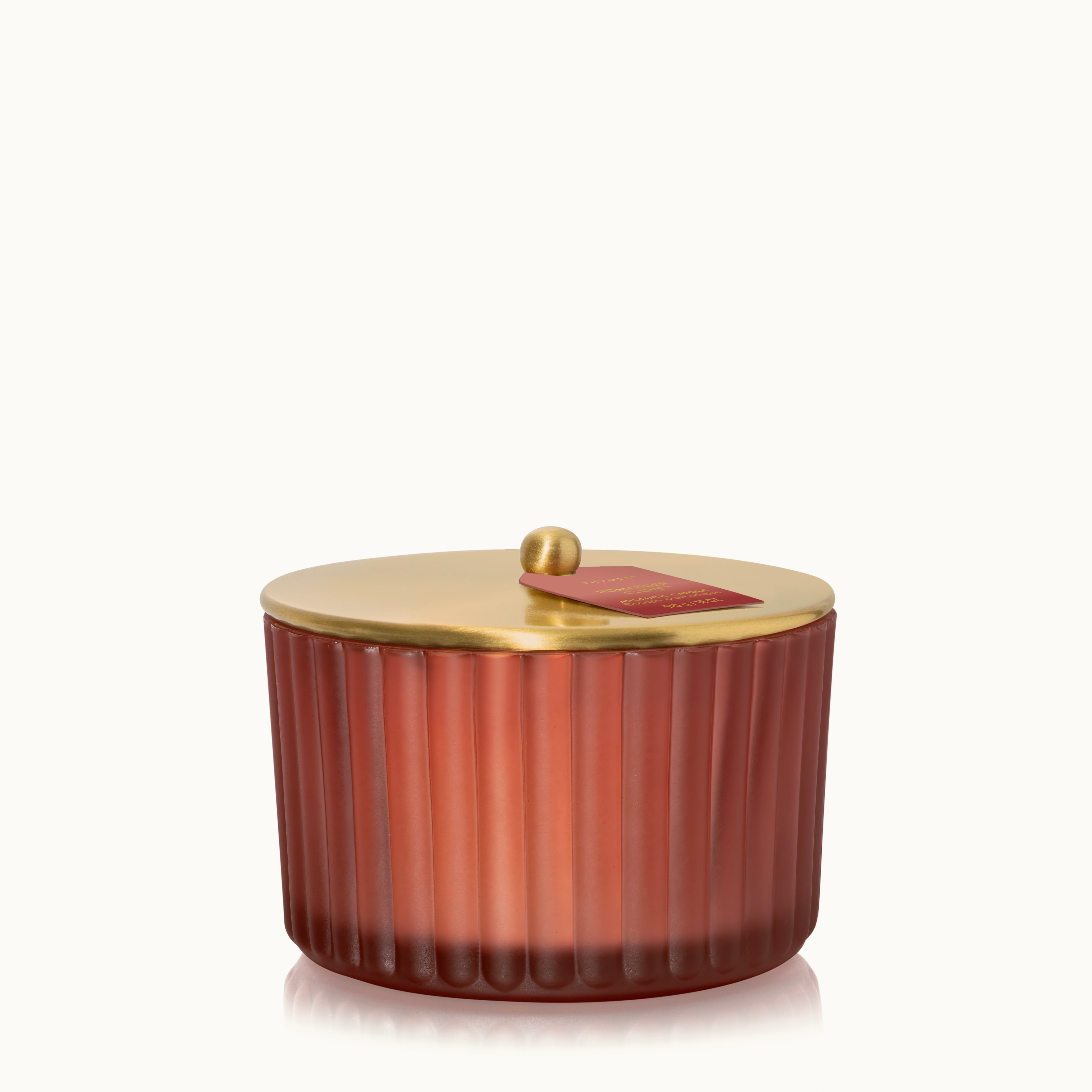 A frosted, matte, sienna orange glass 3 Wick candle with it's metallic, gold finish lid.