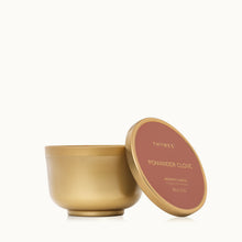 A gold metallic finish candle tin with its lid resting against it.