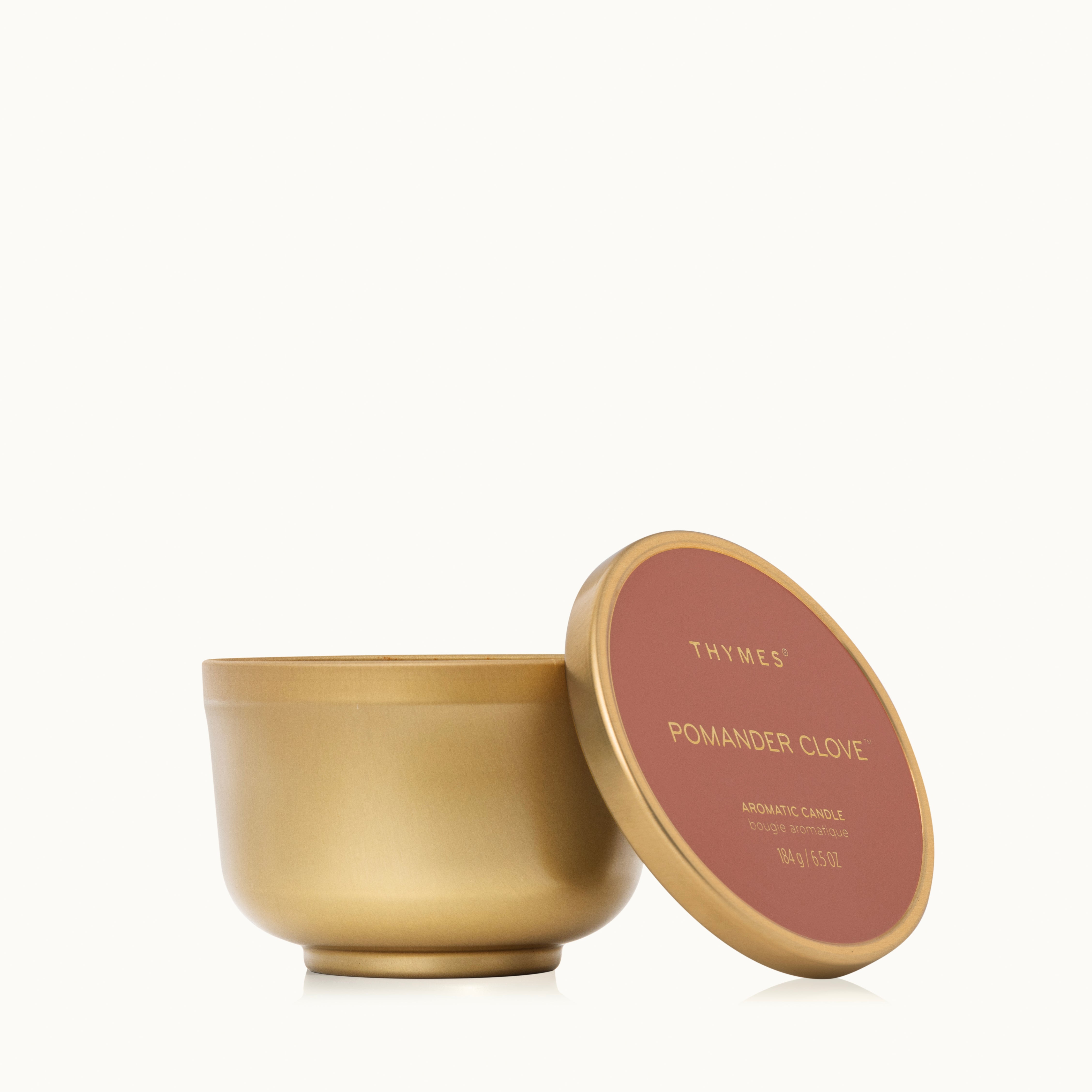 A gold metallic finish candle tin with its lid resting against it.