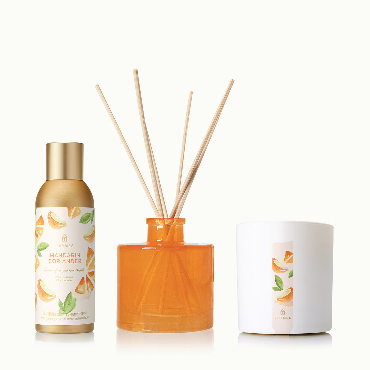 Set of diffuser bottle, orange diffuser with sticks, and candle on a white background
