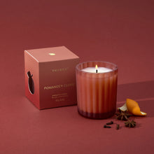A lit 6.1 ounce candle in a frosted, matte glass vessel sits beside its packaging box, whole cloves, star anise and a mandarin peel.