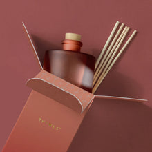 A frosted, matte, sienna orange glass reed diffuser bottle with six reeds presented in its open packaging