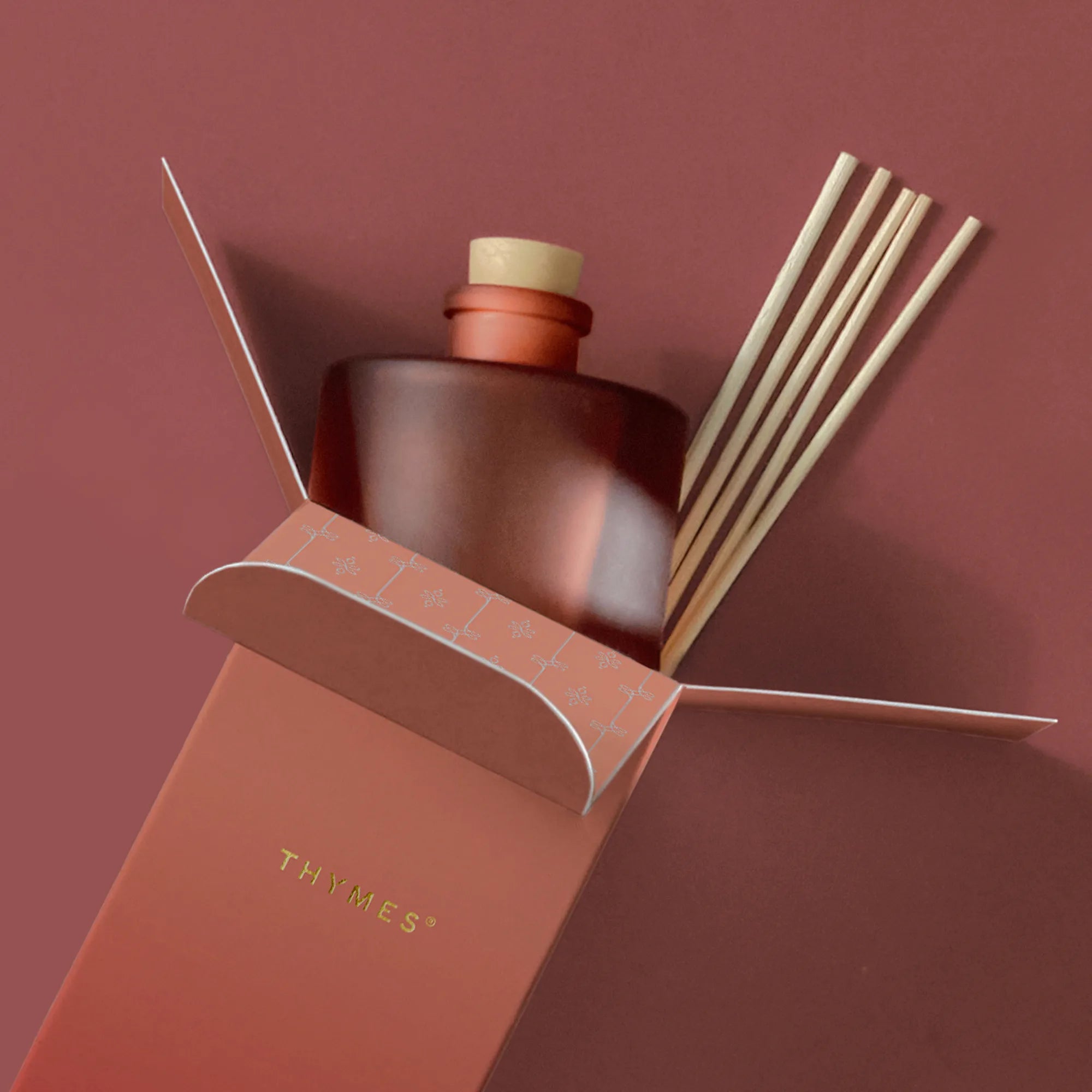 A frosted, matte, sienna orange glass reed diffuser bottle with six reeds presented in its open packaging