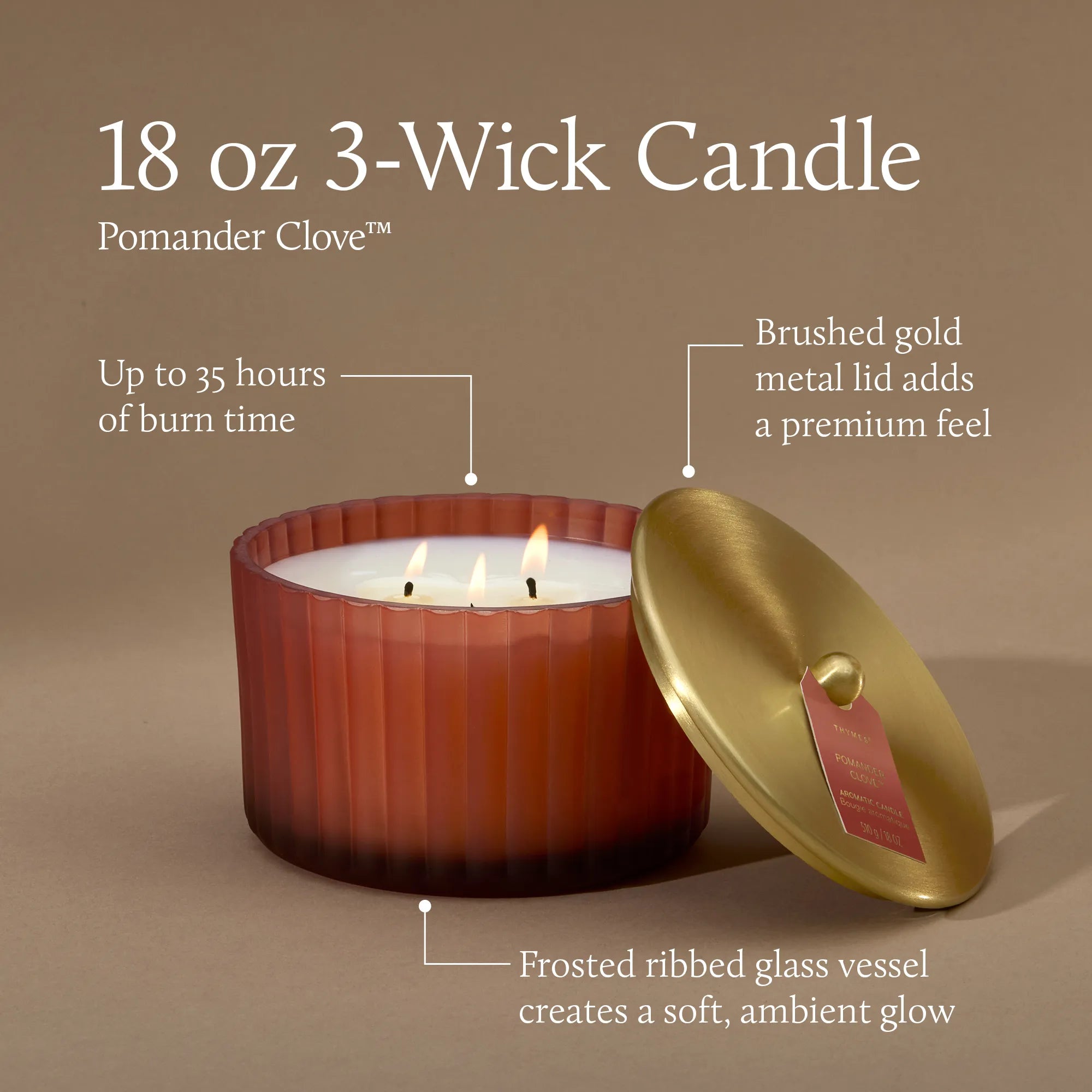 A lit 18 ounce 3 wick candle in a frosted, matte, sienna orange glass vessel with text indicating up to 35 hours of burn time, a brushed gold metal lid that adds a premium feel and a frosted ribbed glass vessel that creates a soft ambient glow.