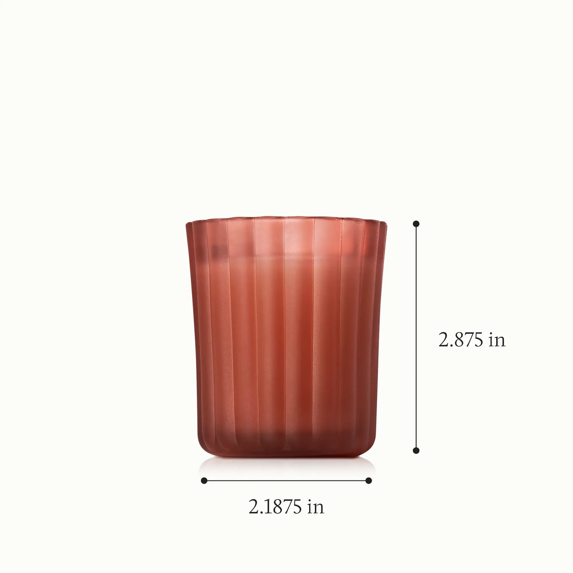 A votive candle in a frosted, matte, sienna orange glass vessel with a height of 2.875 inches and a diameter of 2.1875 inches.